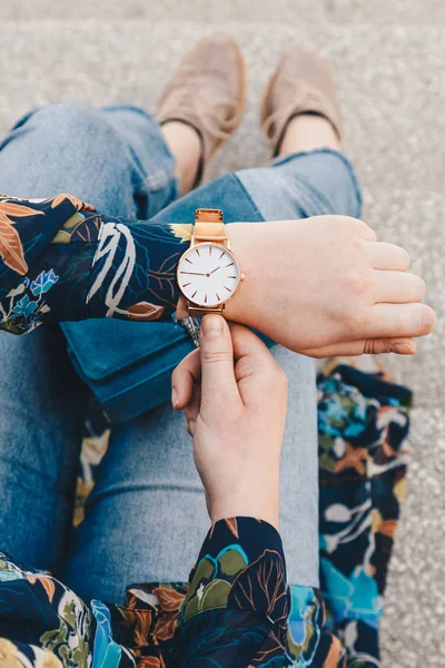 street style fashion details. close up, young fashion blogger wearing a floral jacket, and a white and golden analog wrist watch. checking the time, holding a beautiful suede leather purse.