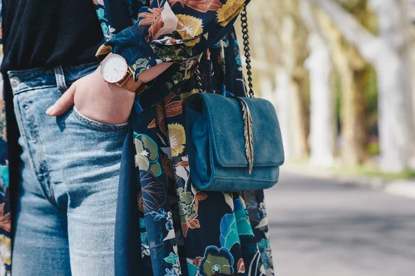 street style fashion details. close up, young fashion blogger wearing a floral jacket, and a white and golden analog wrist watch. checking the time, holding a beautiful suede leather purse.