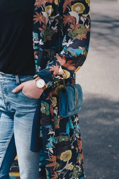 street style fashion details. close up, young fashion blogger wearing a floral jacket, and a white and golden analog wrist watch. checking the time, holding a beautiful suede leather purse.