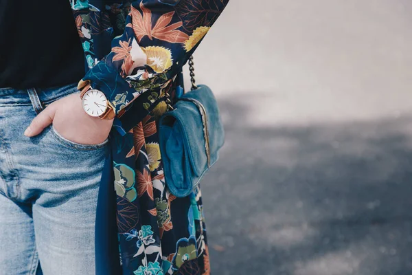 street style fashion details. close up, young fashion blogger wearing a floral jacket, and a white and golden analog wrist watch. checking the time, holding a beautiful suede leather purse.