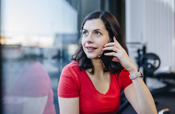 authentic portrait of beautiful fit woman making a phone call in the gym. personal coach talking on smart phone during workout break