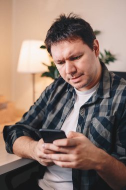 Otantik genç serbest meslek sahibi bir ev ofis oturma onun smartphone üzerinde ciddi ve manifatura süre odaklı olma.