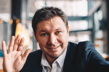 İyi görünümlü genç adam bir kafe barda otururken bir iş video konferans, partaking close-up. O gülümseyen ve kameraya sallayarak. Modern çağın iş dünyasında kavramı.