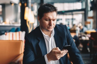 En son iş haberleri ve haberdar kalmak gözatmak için cep telefonunu kullanarak bir restoranda öğle yemeği molası sırasında oturan çekici genç adam.