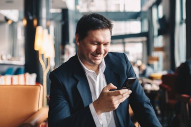 Bir barda oturan yakışıklı genç adam onun cep telefonu sosyal medya üzerinde arkadaşlarınızla metin için bir mola sırasında işten kullanırken gülümseyen.