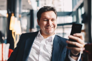 Gülümseyen ve onun Smartphone'da kameraya bakarak görüntülü arama sırasında bir ara iş, kafe barda sahip çekici genç adam Close-Up.