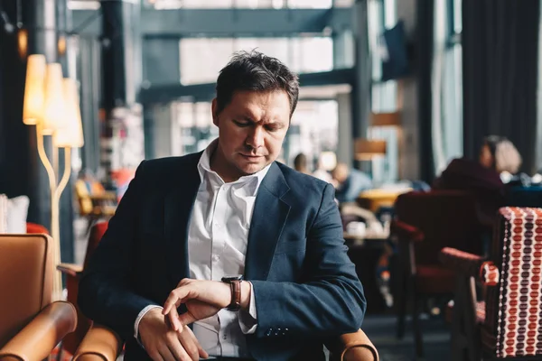 Close-up of good looking young man sitting in a cafe bar, looking at his hand watch like he\'s waiting for someone to come and have a business meeting with. Concept of time is money.