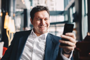 Süre oturan bir kafe barda iş bir mola sırasında gülümseyen ve kameraya cep telefonundan arayan bir selfie alarak çekici genç işadamı Close-Up.