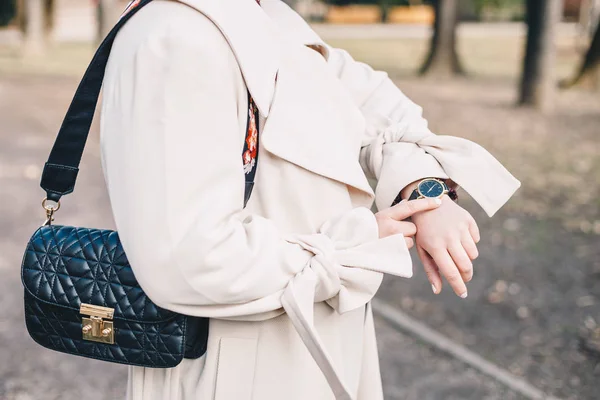 白いオーバー コートで 若い女性のクローズ アップは 彼女の腕時計で時間をチェックし 黒い服を着てキルティング ハンドバッグ — ストック写真