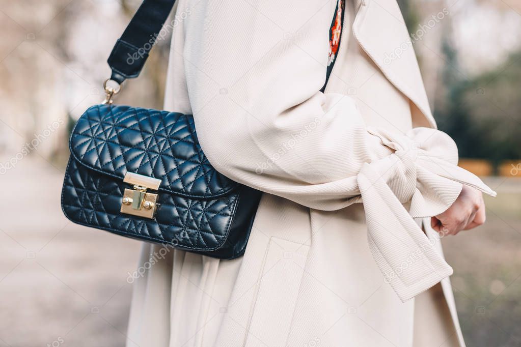 Closeup of a black quilted handbag hanging from the shoulder of a young woman wearing a white coat.