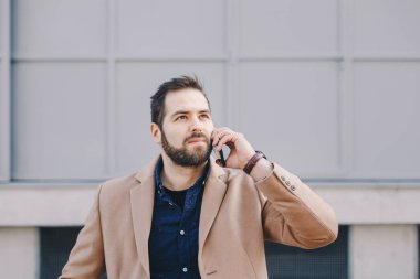 Cep telefonundan bir binanın önünde duran bir kesinti sırasında konuşan çekici ve modern bir genç adam portresi.