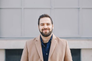 Yakın çekim portre çekici, modern genç adam poz ve kameraya bakarak, moda giysiler giyiyor ve güvenle gülümseyen.