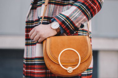 Close-Up moda ayrıntıları, süslü bir deve torba tutarak bir paltosu damalı bir desen ve bir kol saati şık genç moda blogger.