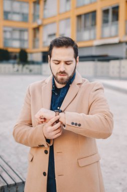 Bir deve chesterfield palto giyiyor, zaman kontrol ve onun analog kol saati üzerinde kemer sıkma yakışıklı genç işadamı.