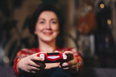 Attractive young woman enjoying free time by playing video games in her living room. Focus on the joystick. clipart