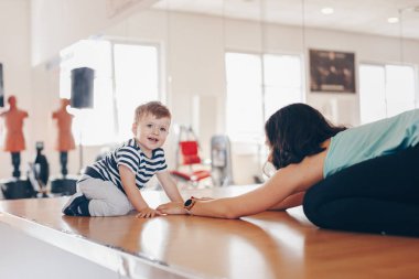 Spor salonunda egzersiz yapan ve onun bebek oğlu ile eğlenmek mutlu genç fit anne Portresi. Sağlıklı yaşam kavramı. Spor, annelik ve aktif konsept.