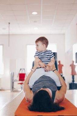 Spor salonunda egzersiz yapan ve onun bebek oğlu ile eğlenmek mutlu genç fit anne Portresi. Sağlıklı yaşam kavramı. Spor, annelik ve aktif konsept.