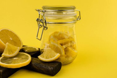 Taze limonlar, cam bir kavanozla sarı bir zemin üzerinde tahta kesme tahtasının üzerinde uzanır.