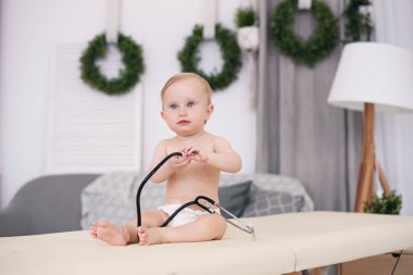 Masaj masasında oturan ve modern tıbbi ofis stetoskop ile oynarken komik küçük bebek.