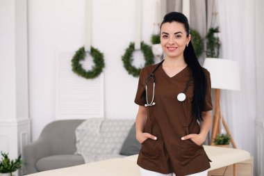 Kameraya bakarak ve modern tıbbi ofis masaj masa arkasında, stetoskop ile gülümseyen genç kadın doktor. Sağlık ve tıp kavramı.