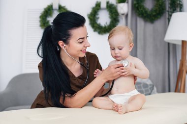 Modern tıbbi ofis stetoskop ile muayene küçük bebek gülümseyen genç doktor.