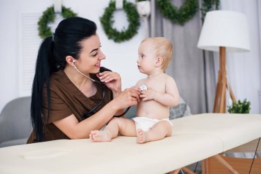Modern tıbbi ofis stetoskop ile muayene küçük bebek gülümseyen genç doktor.