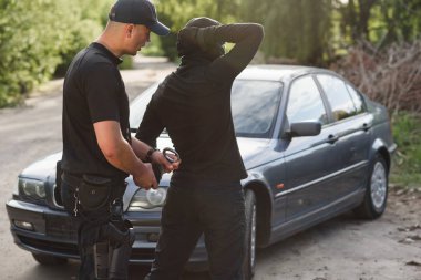 Bir polis memuru çalıntı araba ile bir suçlunun tutuklandı ve onu kelepçeli yakın.
