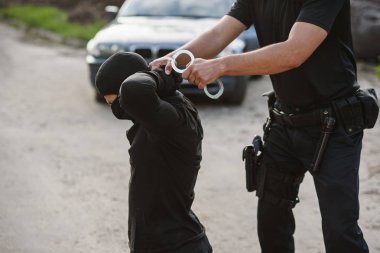 Tutuklanan suçlu diz çökmüş ve polis ona kelepçe takıyor. Kanun ve düzen.