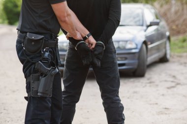 Bir polis memuru çalıntı araba ile bir suçlunun tutuklandı ve onu kelepçeli yakın.