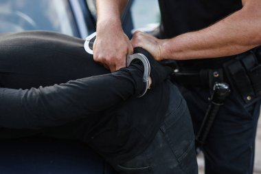 Bir polis memuru çalıntı bir araba ile maskeli suçlu tutuklandı ve onu arabanın kaputuna kelepçeli.