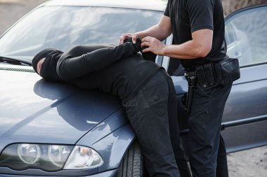 Bir polis memuru çalıntı bir araba ile maskeli suçlu tutuklandı ve onu arabanın kaputuna kelepçeli.