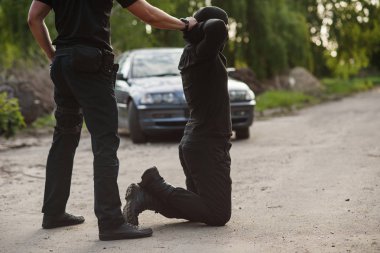 Tutuklanan suçlu diz çökmüş ve polis ona kelepçe takıyor. Kanun ve düzen.