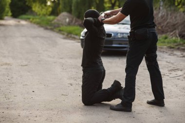Tutuklanan suçlu diz çökmüş ve polis ona kelepçe takıyor. Kanun ve düzen.