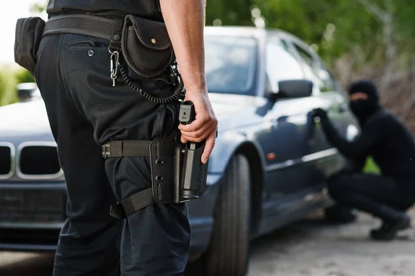 A policeman with a hand gun in his hand arrested a criminal who stole a car. Law and justice.
