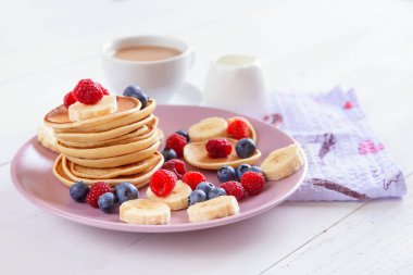 Beyaz bir arka plan üzerinde mor bir tabak içinde taze çilek ile lezzetli ev yapımı kek. Ahududu, yaban mersini ve muz krep lezzetli ve sağlıklı bir kahvaltı. Sütlü aromatik kahve.