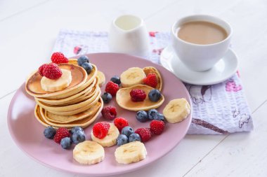 Beyaz bir arka plan üzerinde mor bir tabak içinde taze çilek ile lezzetli ev yapımı kek. Ahududu, yaban mersini ve muz krep lezzetli ve sağlıklı bir kahvaltı. Sütlü aromatik kahve.