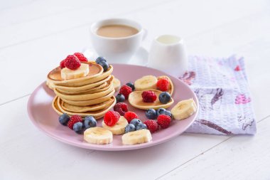 Beyaz bir arka plan üzerinde mor bir tabak içinde taze çilek ile lezzetli ev yapımı kek. Ahududu, yaban mersini ve muz krep lezzetli ve sağlıklı bir kahvaltı. Sütlü aromatik kahve.