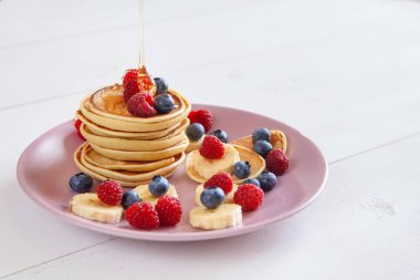 Beyaz bir arka plan üzerinde mor bir tabak içinde taze çilek ile lezzetli ev yapımı kek. Ahududu, yaban mersini ve ballı krep lezzetli ve sağlıklı bir kahvaltı.