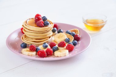 Beyaz bir arka plan üzerinde mor bir tabak içinde taze çilek ile lezzetli ev yapımı kek. Ahududu, yaban mersini ve ballı krep lezzetli ve sağlıklı bir kahvaltı.