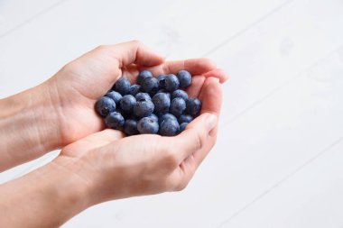 Beyaz ahşap zemin üzerinde kadın elinde taze yaban mersini. Üstten görünüm.