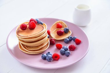 Beyaz bir arka plan üzerinde mor bir tabak içinde taze çilek ile ev yapımı lezzetli gözleme. Krep ahududu, yaban mersini ve taze süt ile lezzetli ve sağlıklı bir kahvaltı.