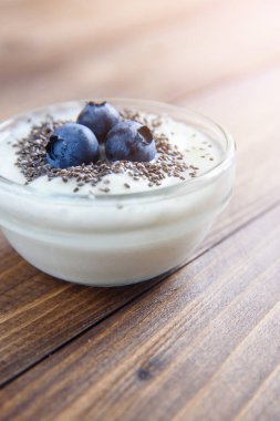 Saydam bir cam chia tohum ve ahşap arka plan üzerinde yaban mersini ile yoğurt.