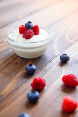 Saydam bir cam ile taze yaban mersini ve ahududu ahşap bir zemin üzerine yoğurt.