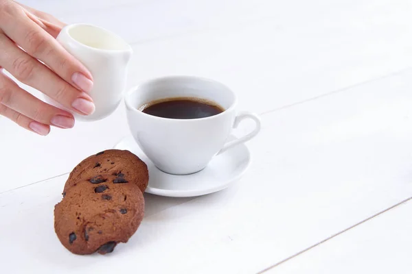女性の手は コーヒーに牛乳を注ぐ 香り豊かなコーヒーと白い背景の上のクッキーのカップ — ストック写真
