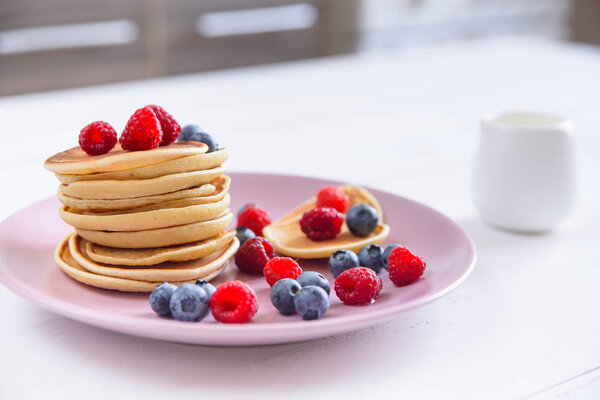 Delicious homemade pancakes with fresh berries in a violet plate on a white background. A tasty and healthy breakfast of pancakes with raspberries, blueberries and honey.