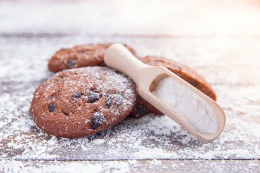 Ahşap zemin üzerine çikolata parçaları kurabiye kurabiye ile pudra şekeri serpilir. Taze hamur işi. Tanımlama bilgileri, pudra şekeri ve ahşap bir ölçme kaşık yapma işlemi çalışma.