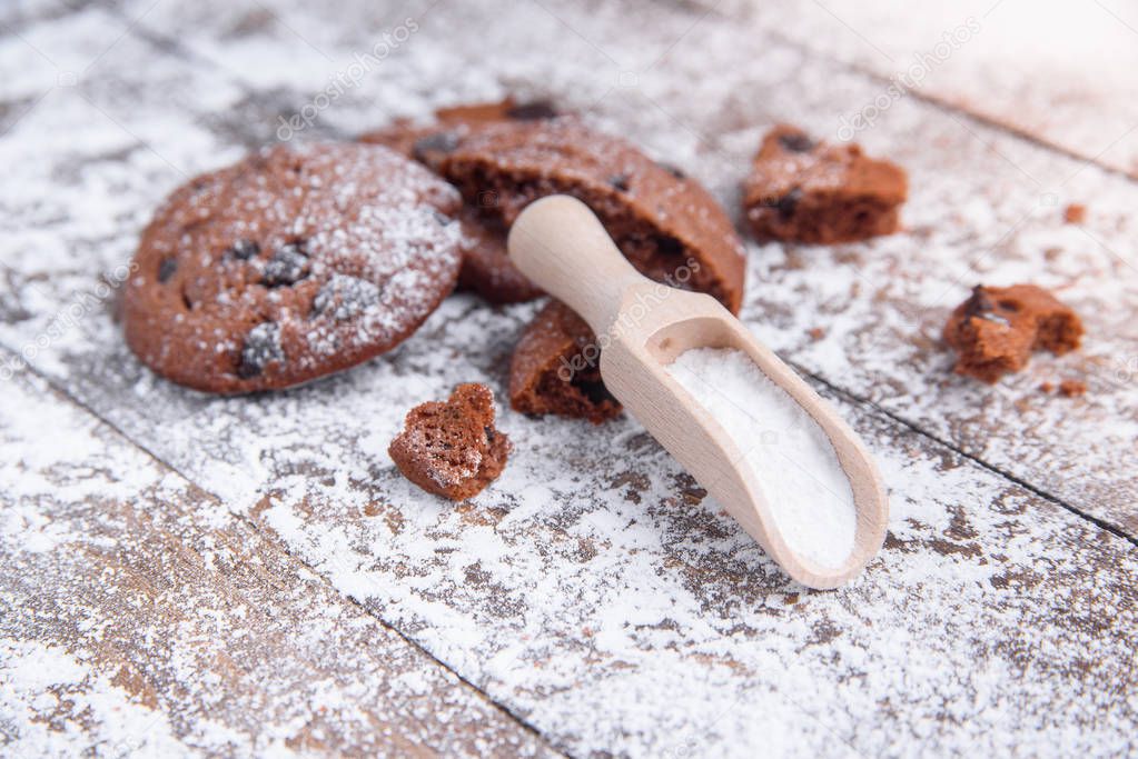 Cookies with chocolate slices sprinkled with powdered sugar and a wooden measuring spoon. Fresh pastry on wooden background.