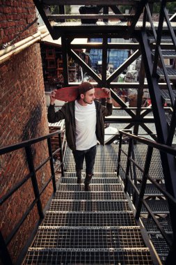 Genç yakışıklı hipster adam siyah demir merdiven endüstriyel bina kaykay ile.