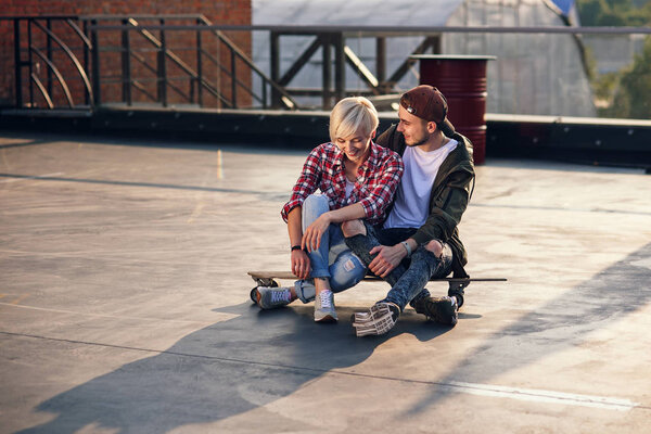 Young lovely couple having fun with longboard skateboard on the roof of industrial building. Modern urban active lifestyle concept.