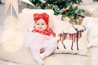 Yazdırılan bir geyik arka planda bir Noel ağacı ve hediye tatil yastıkla yakınındaki şenlikli elbiseli küçük komik kız.